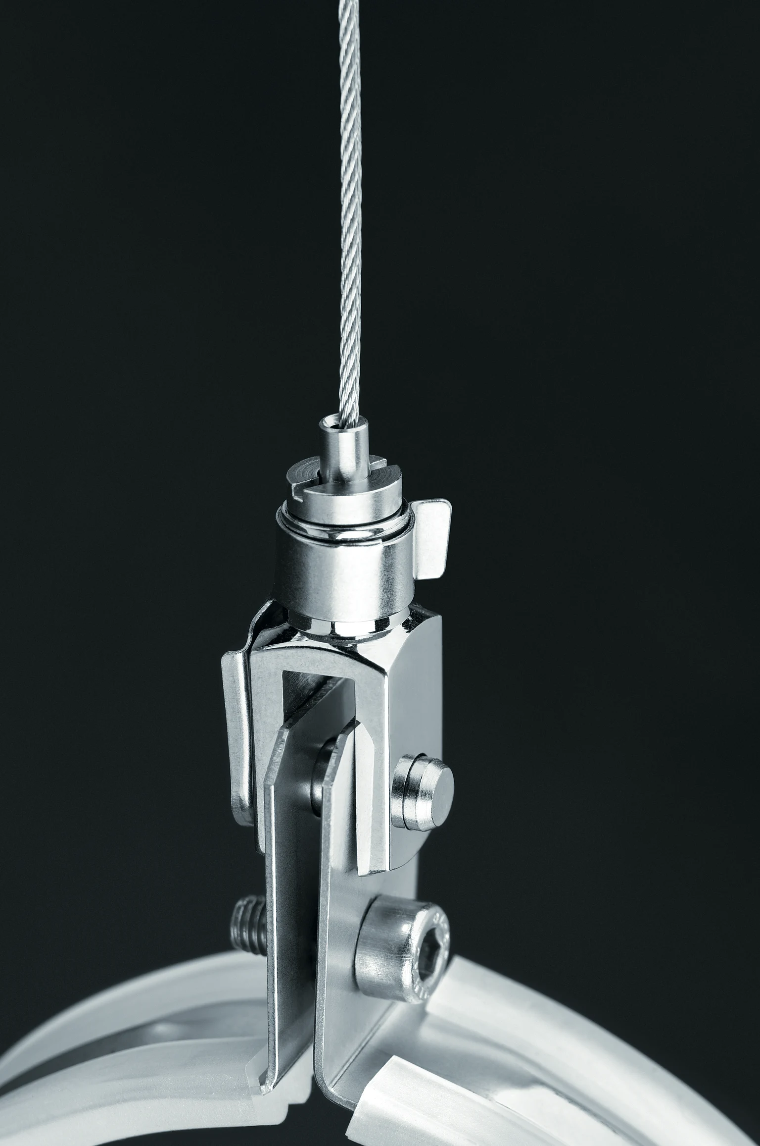  L'immagine mostra nei dettagli il sistema di sospensione del sistema di illuminazione TUBILUX con un robusto fissaggio a cavo metallico su uno sfondo neutro.