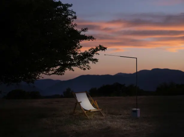 Image d'application de la marque Diomede avec un luminaire dans le jardin et une chaise longue sous un arbre, éclairé au crépuscule