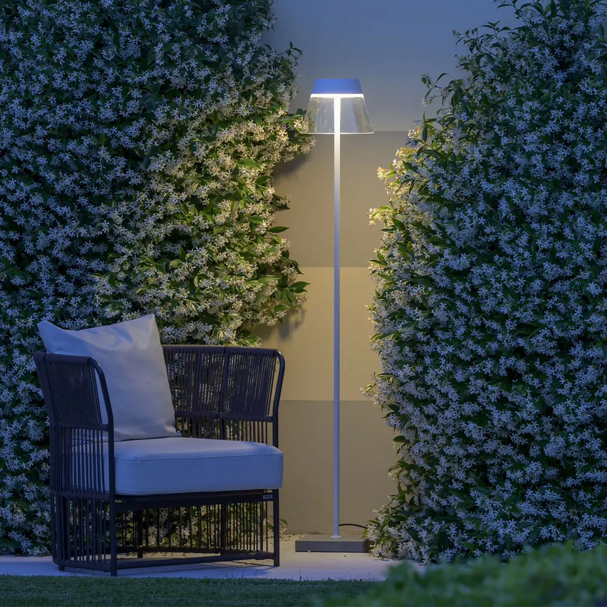 Outdoor Stehleuchte Pragma Outdoor von Ghidini beleuchtet einen Stuhl vor einer Gartenhecke