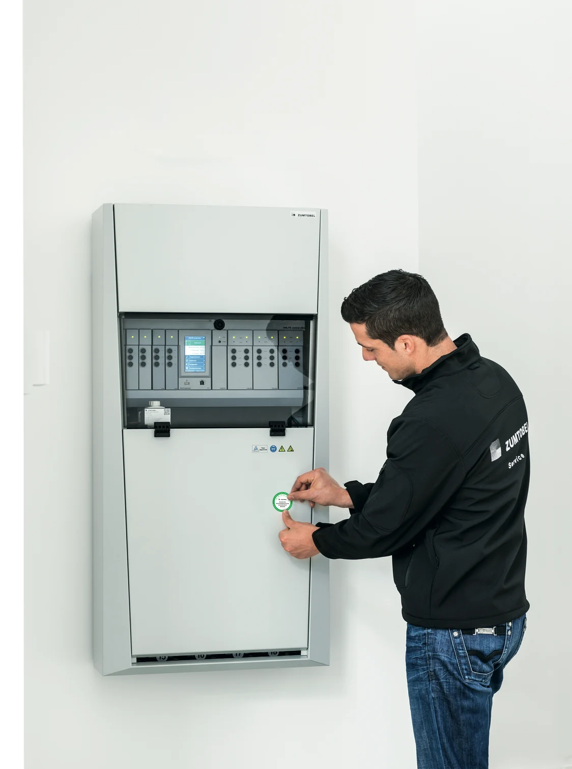  A person is working on the ONLITE central eBox, which is mounted on a white wall, in a technical room for lighting control.