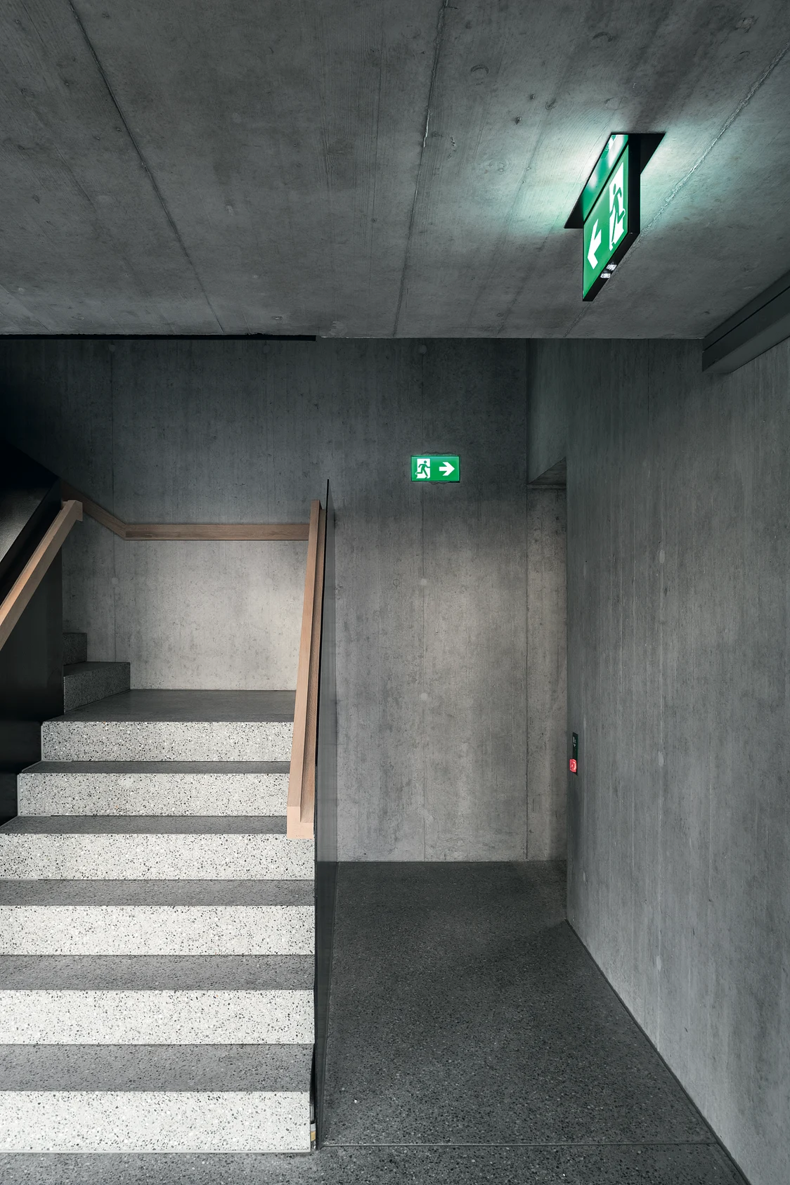 The PURESIGN emergency luminaire in a modern concrete staircase within a minimalist stairwell.