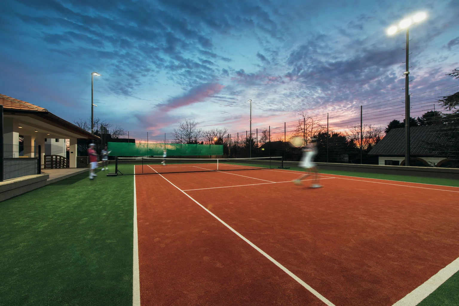 Un court de tennis avec un joueur qui sert la balle pendant un match en soirée.