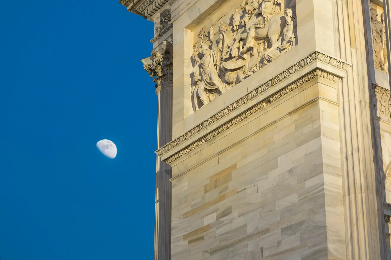 Gros plan de lArc de triomphe du Simplon montrant des détails des pierres sculptées, avec la lune brillant en arrière-plan.