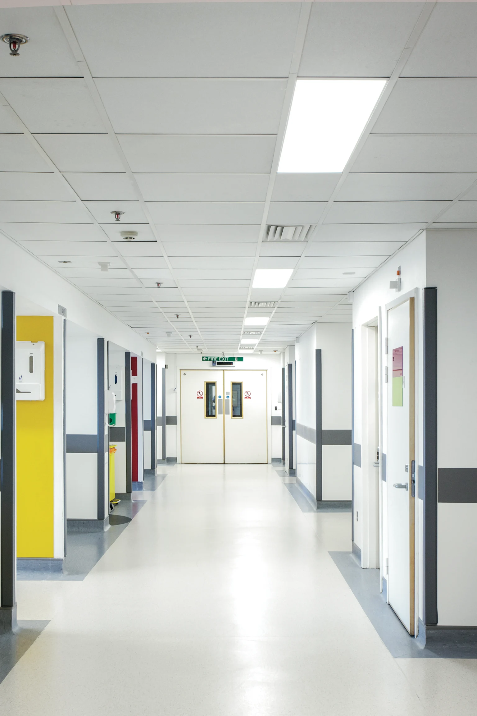 Helder verlichte ziekenhuisgang met gepolijste vloeren, witte muren en led-paneelverlichting aan het plafond.