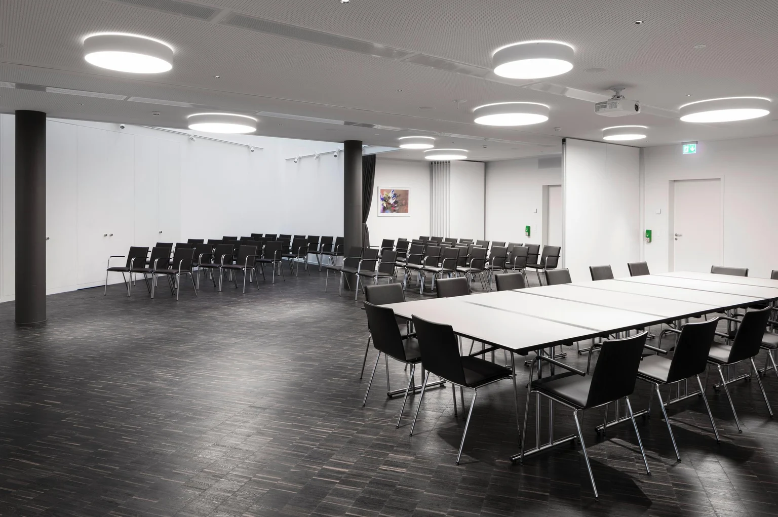 Una sala conferenze vuota con tavoli e sedie, allestita per un evento. Il design luminoso e l'illuminazione moderna creano un'atmosfera professionale.