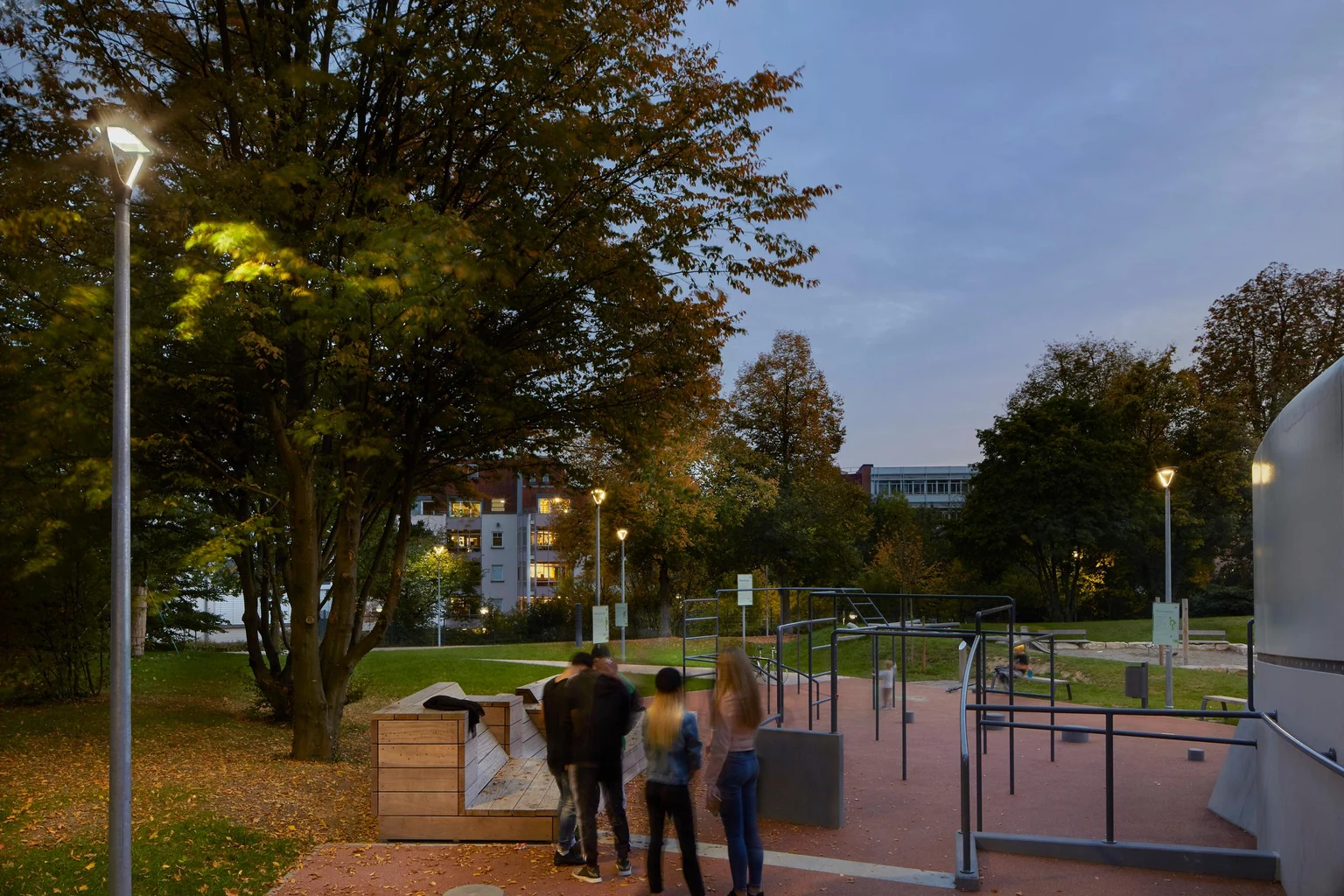 Mensen verzamelen zich bij fitnessapparatuur in een park, waarbij de verlichting zorgt voor goede zichtbaarheid en een uitnodigende sfeer.