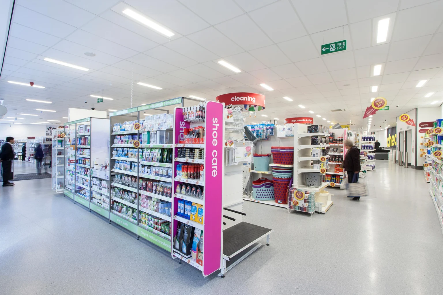 Une allée de supermarché bien éclairée avec des étagères remplies de produits de nettoyage et d’articles ménagers. La signalétique des sections, par exemple « nettoyage », aide à organiser l’espace, tandis que la disposition ouverte facilite l’orientation.