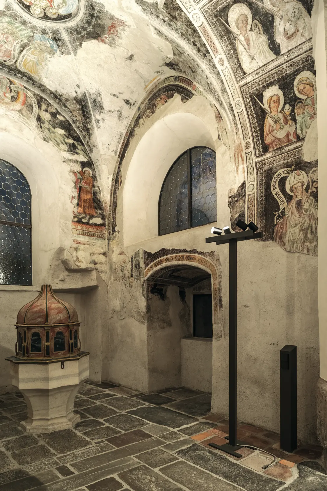 Die Wand- und Deckenmalereien werden durch gerichtete Strahler dezent und blendfrei hervorgehoben, Tageslicht dringt nur schwach ein.