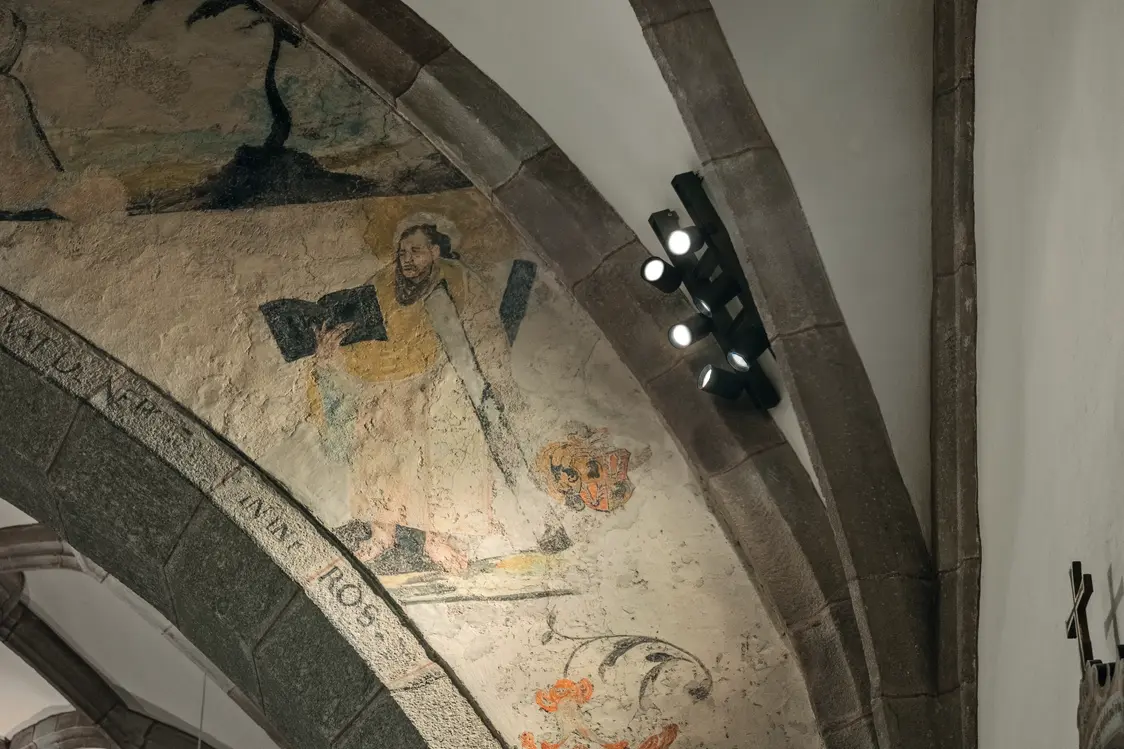 Mehrere Strahler setzen gezielte Lichtakzente auf das Wandgemälde und sorgen für eine betonte, helle Ausleuchtung.