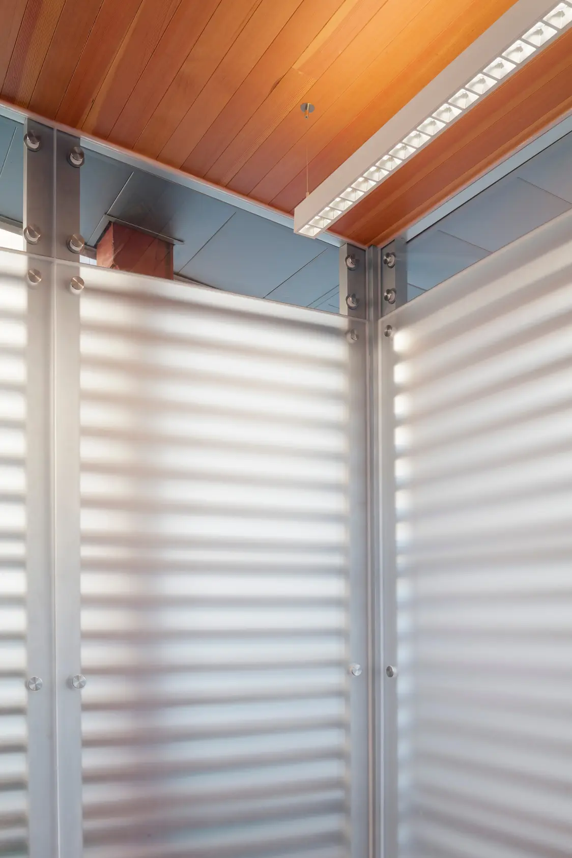 Die lineare LED-Leuchte an der Decke sorgt für blendfreies, gleichmäßiges Licht, während die transluzenten Lamellen das Tageslicht weich streuen und für Privatsphäre sorgen.