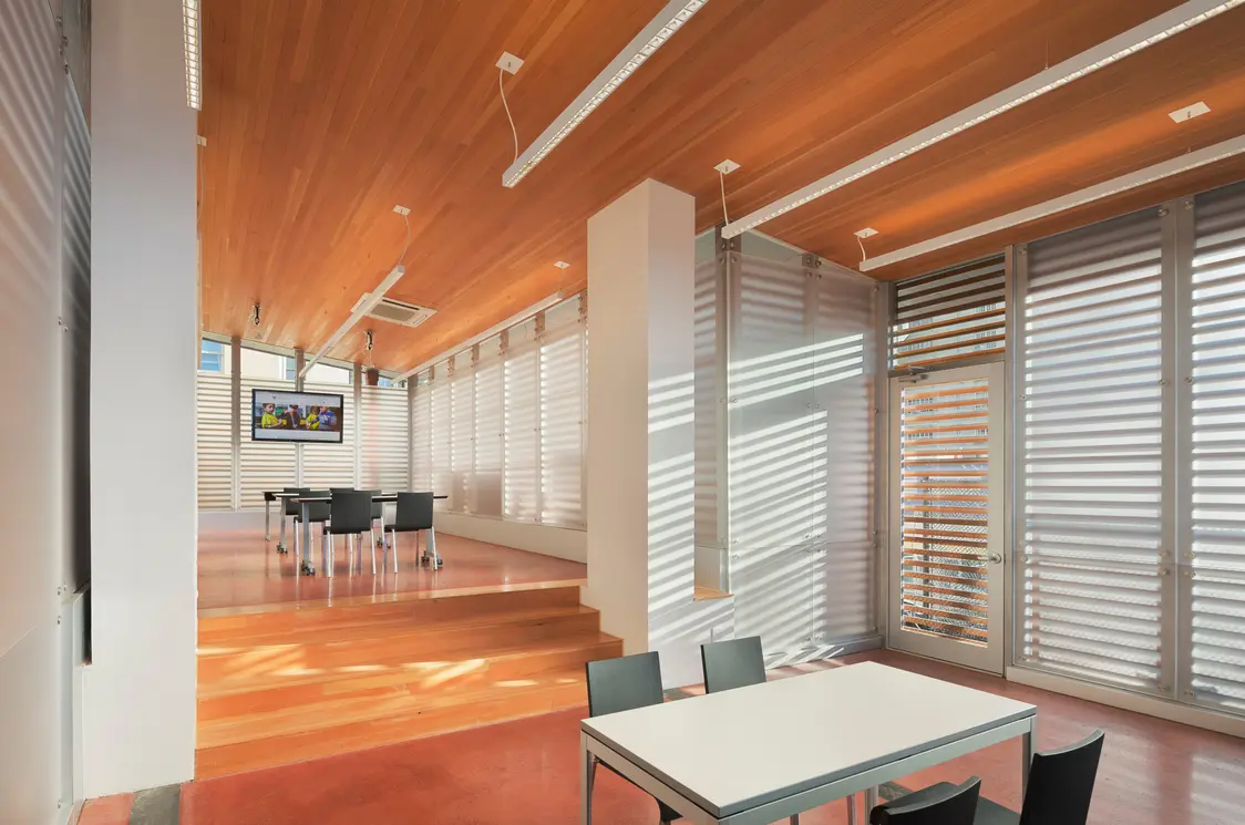 Die linearen LED-Leuchten in der Holzdecke sorgen für eine gleichmäßige Ausleuchtung des Raumes. Die Lamellen an den Fenstern lassen viel Tageslicht herein, verhindern aber Blendung und schaffen so ein angenehmes Raumklima.