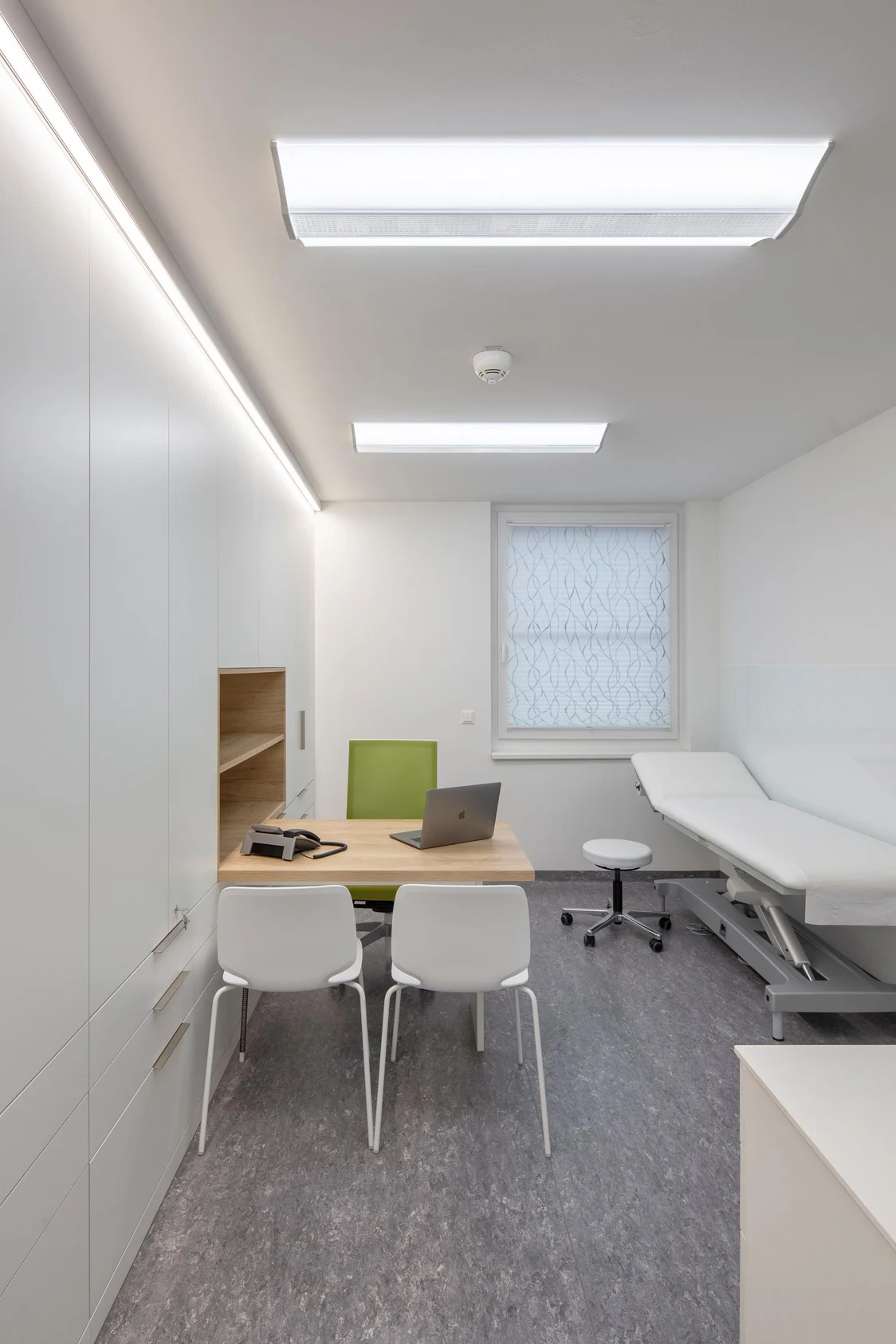 MELLOW LIGHT éclaire uniformément une salle de traitement moderne avec une fenêtre, une table, des chaises et une table d’examen.