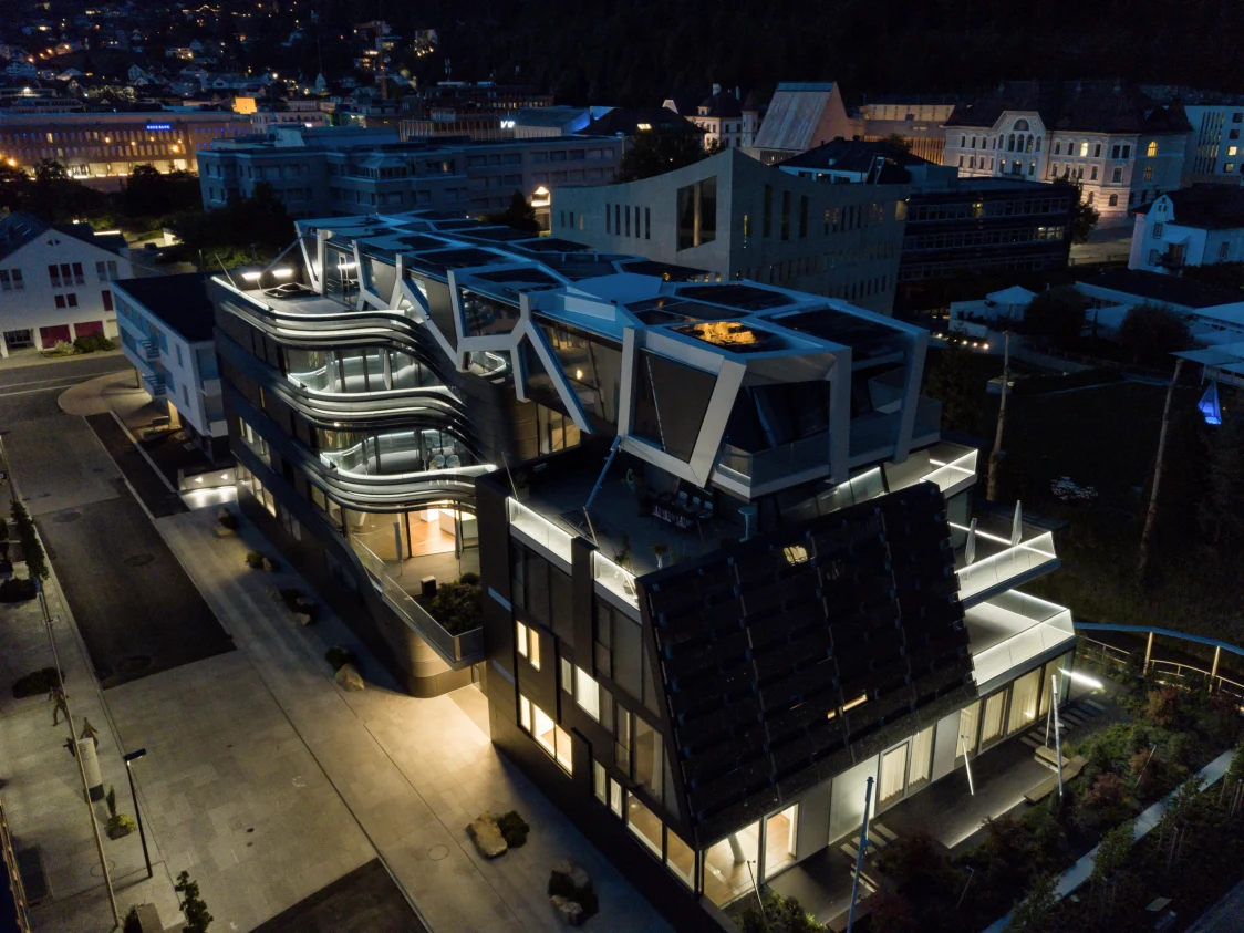 Luftaufnahme eines modernen, beleuchteten Bürogebäudes in der Nacht. Das Gebäude zeichnet sich durch geschwungene Linien und einzigartige architektonische Elemente aus.