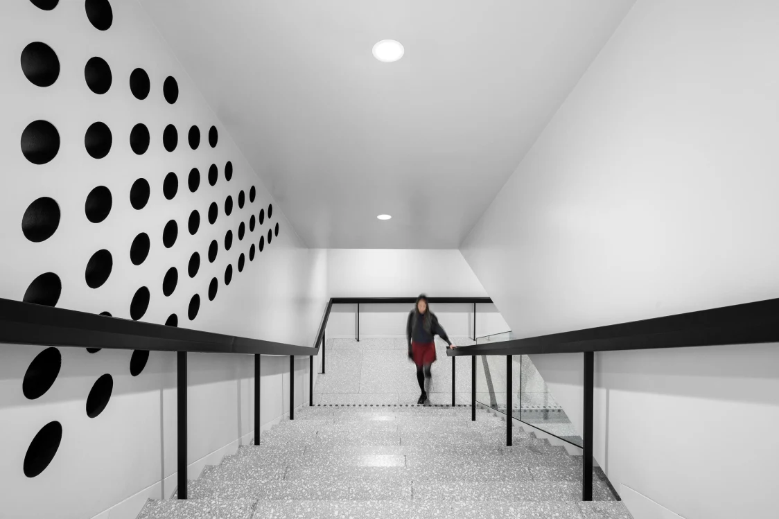 Staircase with a white wall design, black circular motifs, and integrated ceiling lighting. The clear lighting design ensures safety and highlights the graphic design concept