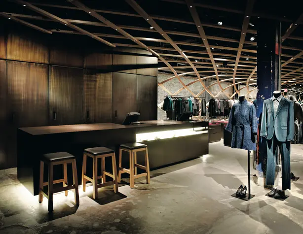 Ein Kleidungsgeschäft mit einer Bar und Barhockern, dazu viele Kleiderständer und Schaufensterpuppen