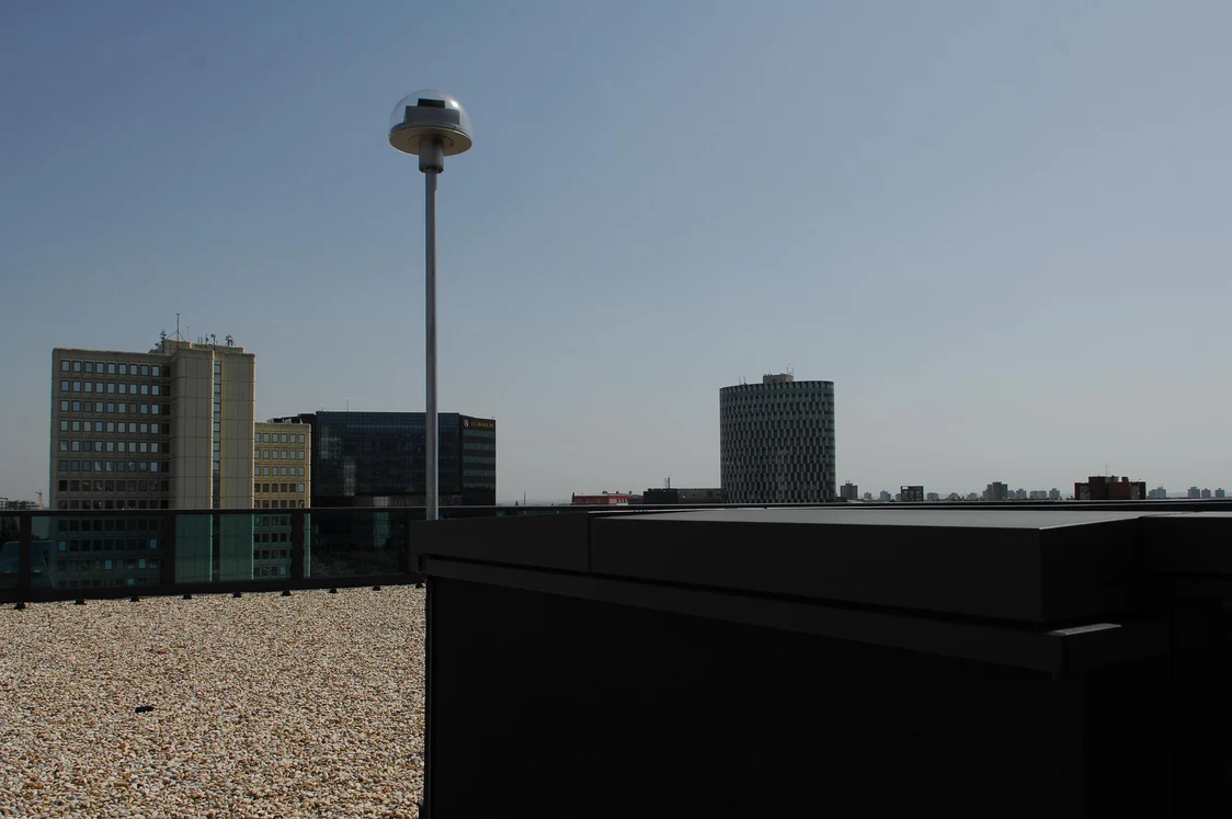 Un capteur de lumière naturelle LITENET est installé sur un toit gravillonné, entouré d’immeubles de bureaux baignant dans la lumière du jour.