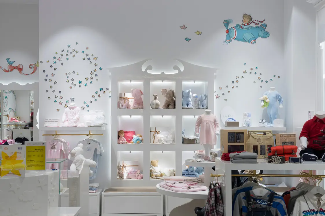 Presentation wall with illuminated compartments, children's clothing, and playful wall motifs; the integrated lighting solution effectively showcases the displayed products.