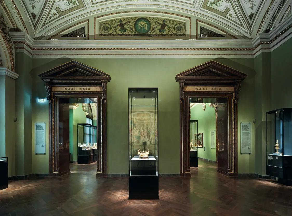 Un hall d’entrée menant aux salles d’exposition avec des murs verts et des encadrements de porte classiques. La vitrine centrale est équipée d’un éclairage LED qui met parfaitement en valeur l’objet exposé et structure l’espace.