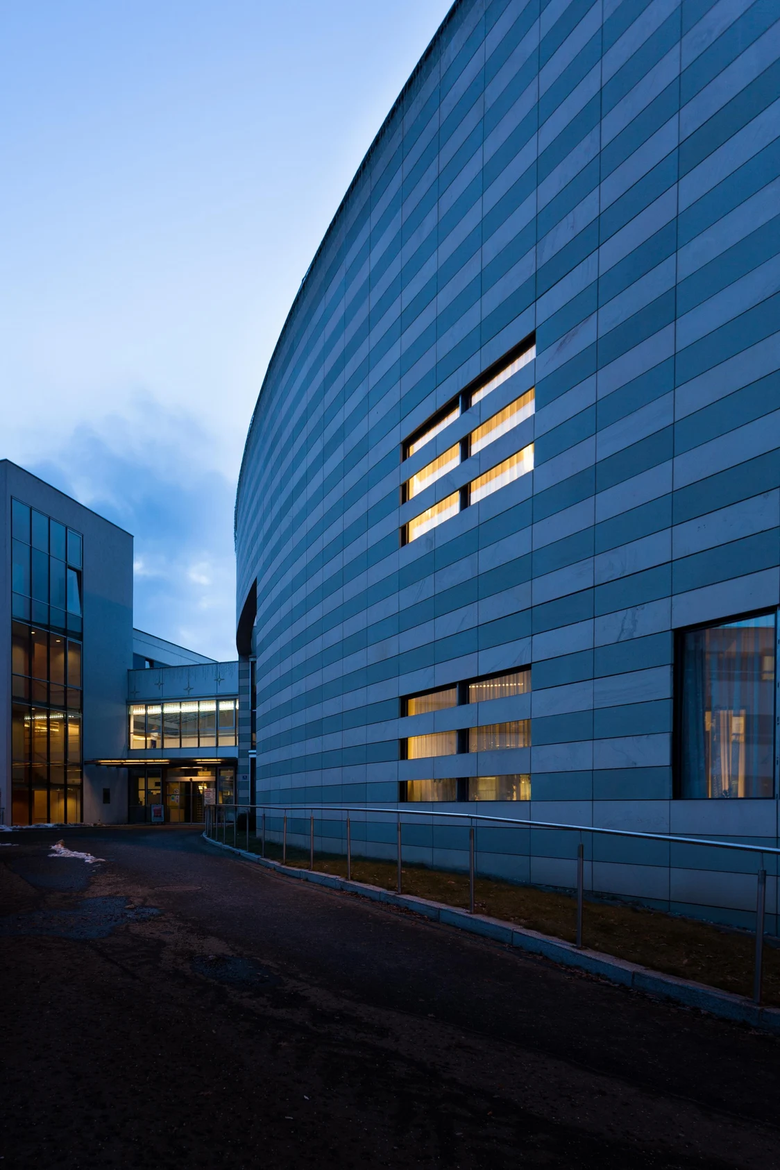 Moderne Krankenhausfassade in Bruck an der Mur bei Abenddämmerung, mit beleuchteten Fenstern und fließender Architektur.