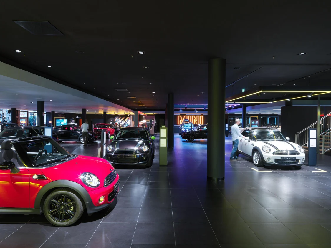 Innenansicht eines MINI-Showrooms mit verschiedenen Fahrzeugen, gezielte Lichtlösung durch Deckenspots hebt die ausgestellten Autos hervor und schafft eine dynamische Atmosphäre.