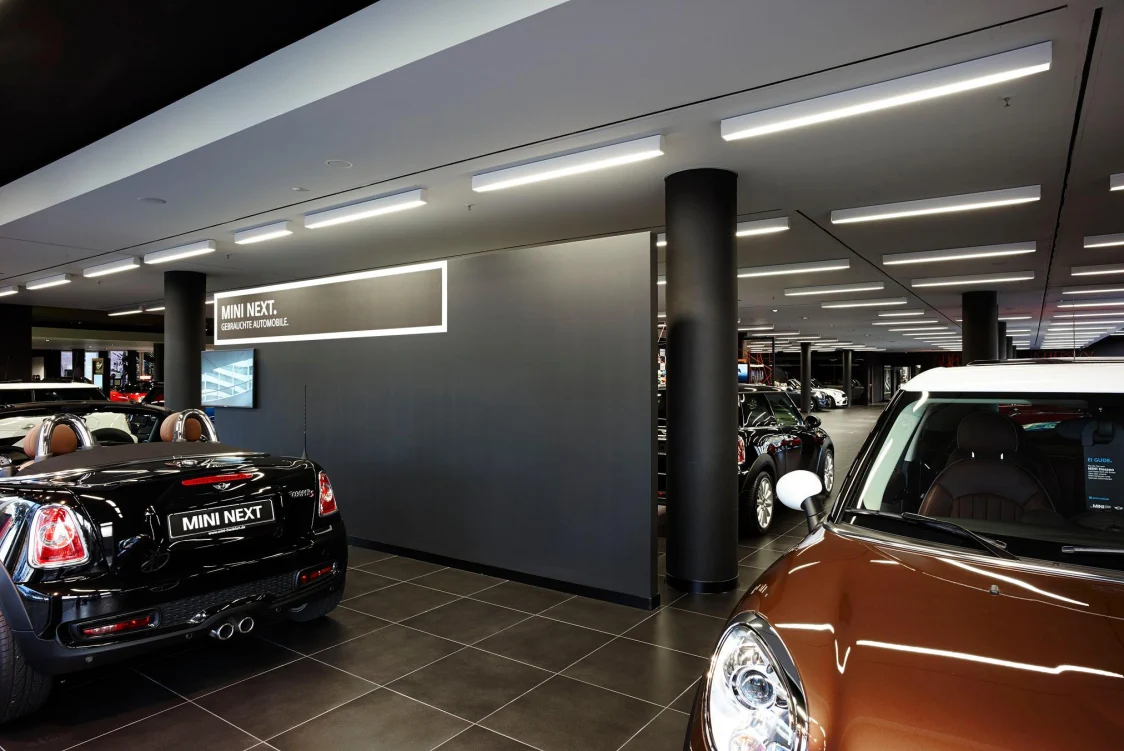 Innenansicht eines MINI-Showrooms mit mehreren Fahrzeugen, lineare Deckenleuchten als Lichtlösung sorgen für eine gleichmäßige, helle Ausleuchtung der Autos.