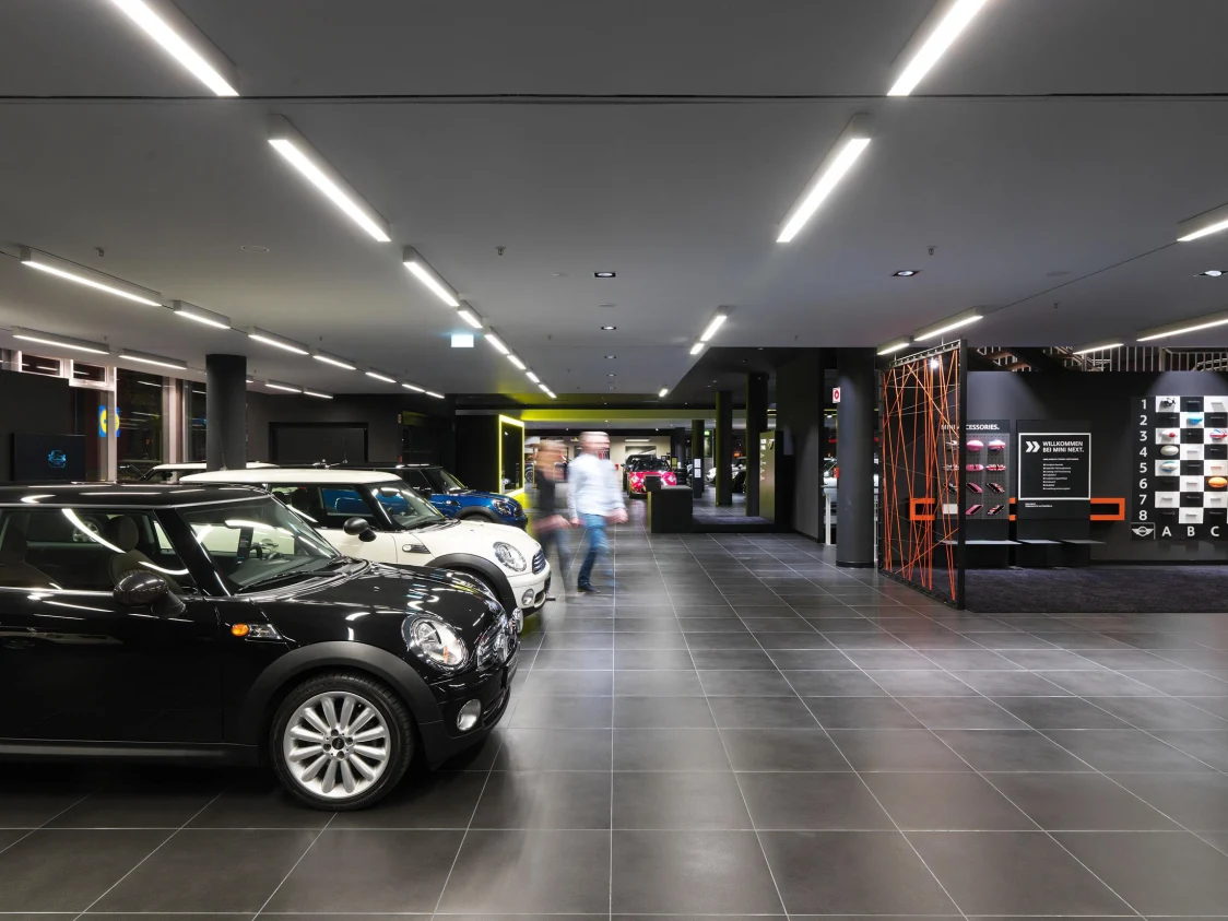 Moderner Autoshowroom mit mehreren MINI-Fahrzeugen, helle lineare Deckenleuchten als Lichtlösung sorgen für eine gleichmäßige und freundliche Ausleuchtung.