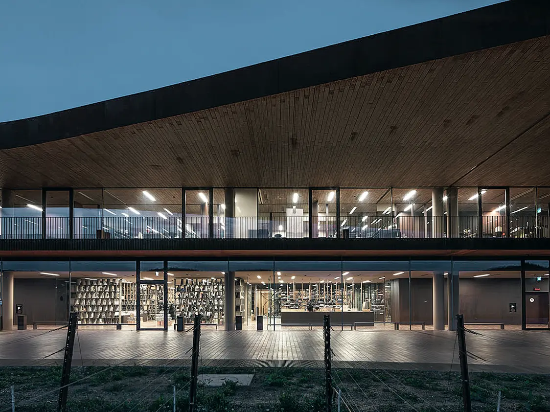A modern building with a striking wooden and large glass façade that illuminate the interior. The open architecture connects the upper and lower levels, creating an inviting atmosphere.