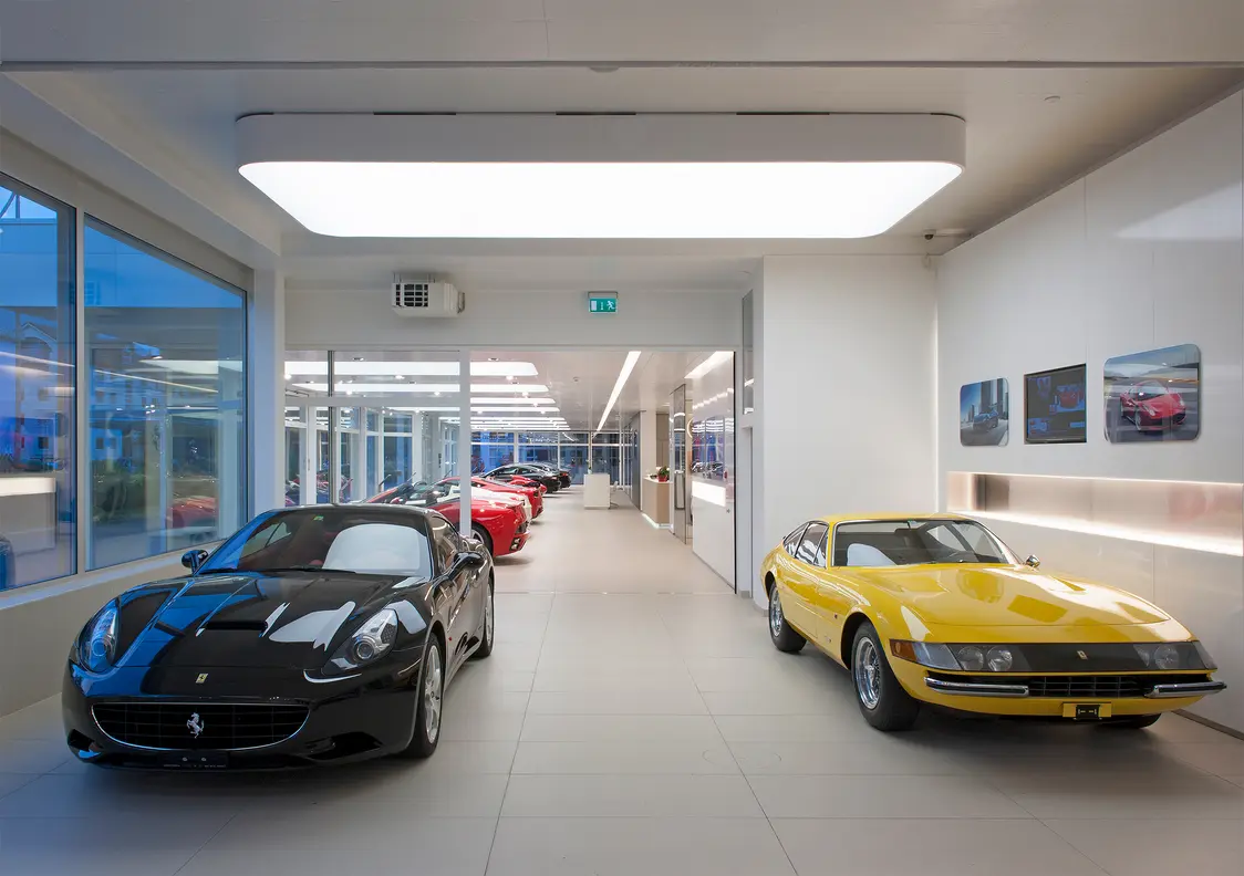 Showroom luminoso con auto sportive nere e gialle; una grande lampada a soffitto garantisce un'illuminazione uniforme e priva di abbagliamenti, mettendo in risalto i veicoli.