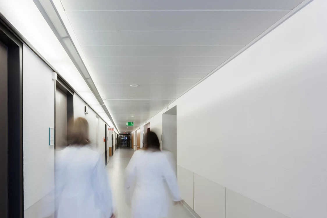 Modern hospital facade in Bruck an der Mur at dusk, featuring illuminated windows and flowing architecture.