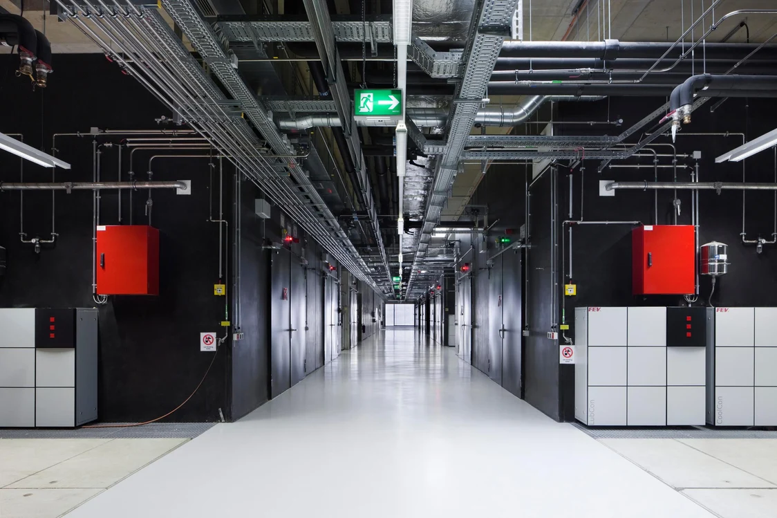 Corridoio tecnico industriale con impianti a vista e sistema di illuminazione lineare TECTON, illuminazione precisa per ambienti di lavoro tecnici.