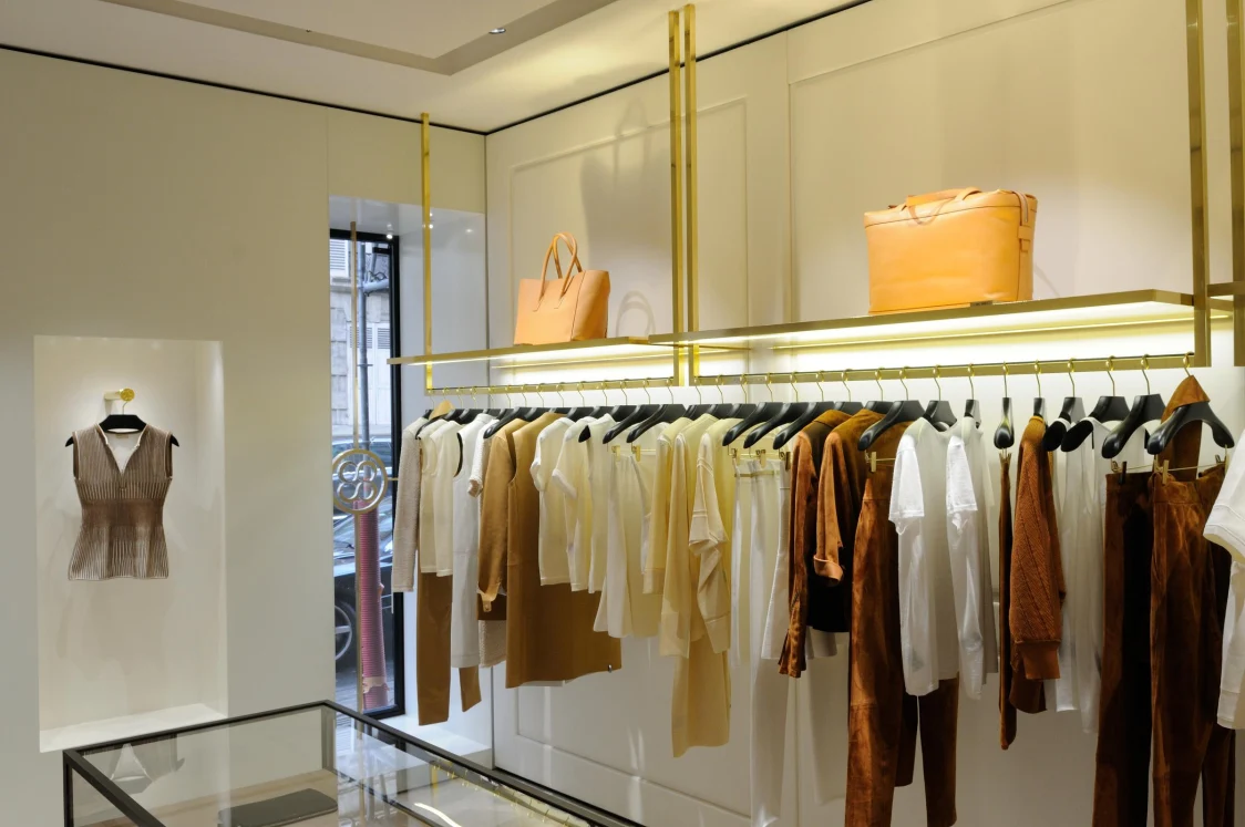Fashion store with large windows and golden details, where daylight and a targeted lighting solution highlight the displayed clothing and accessories.