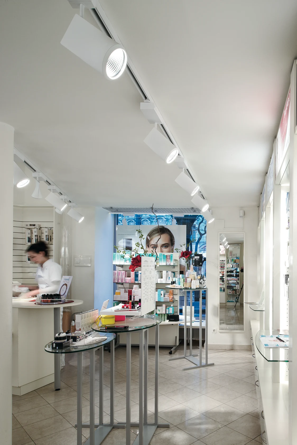 IYON LED-Strahler beleuchtet gleichmäßig einen modernen Kosmetikladen mit hellen Regalen voller Produkte und einem Kundenberater im Hintergrund.