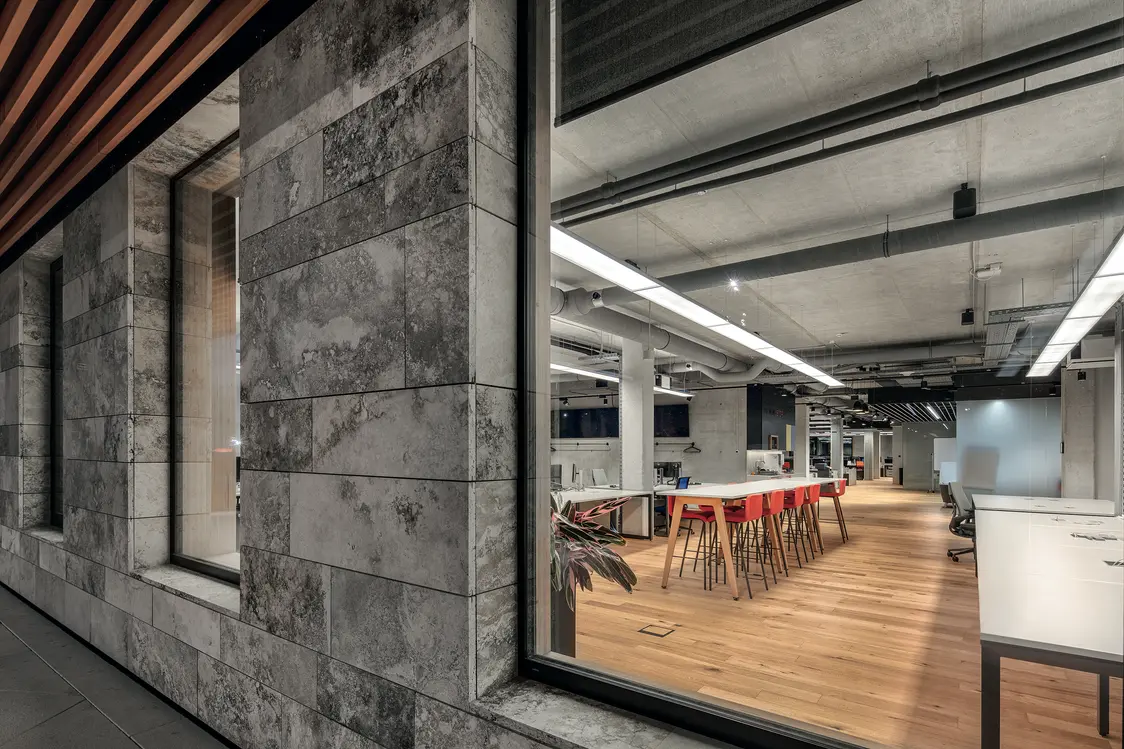 Einblick in ein modernes Büro mit Sichtbetondecke, Holzboden und zentralem Besprechungstisch. Das lineare Lichtsystem betont die klare Architektur und schafft eine helle, fokussierte Arbeitsatmosphäre.