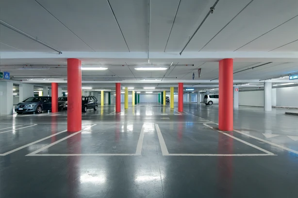 Ein modernes Parkhaus mit neuen LED Leuchten von Zumtobel ausgestatten. in der Mitte sind zwei rote Säulen zu sehen.