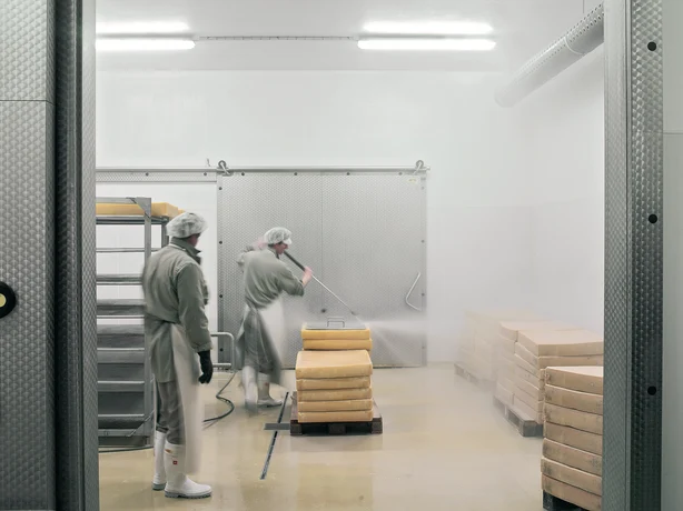 Lebensmittelproduktion hier am Beispiel von Käse, der von zwei Arbeitern gereinigt wird. 