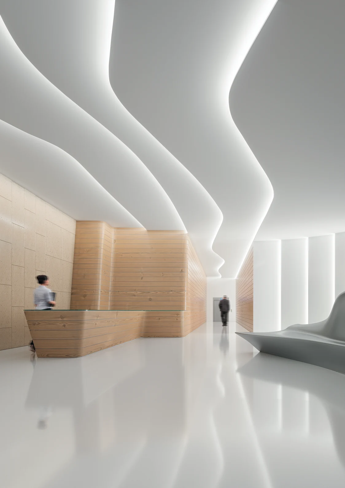 The LINELIGHT lighting system produces gentle, curved lines of light on the ceiling of a modern reception area with wood paneling.