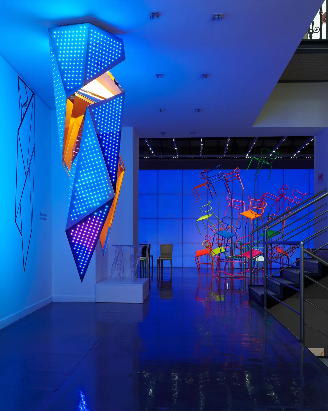 Sculpture lumineuse futuriste à LED bleues de Zumtobel, accompagnée d’installations de chaises colorées