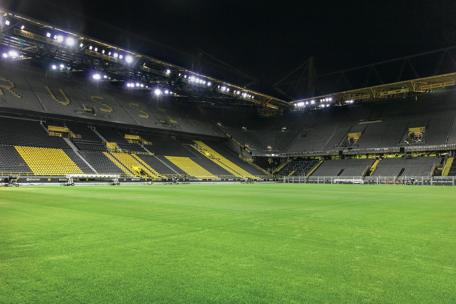 Binnenaanzicht van Signal Iduna Park ´s avonds met het helder verlichte groene speelveld. De iconische gele en zwarte tribunes en de indrukwekkende stalen constructie van het stadion zorgen voor een bijzondere sfeer.