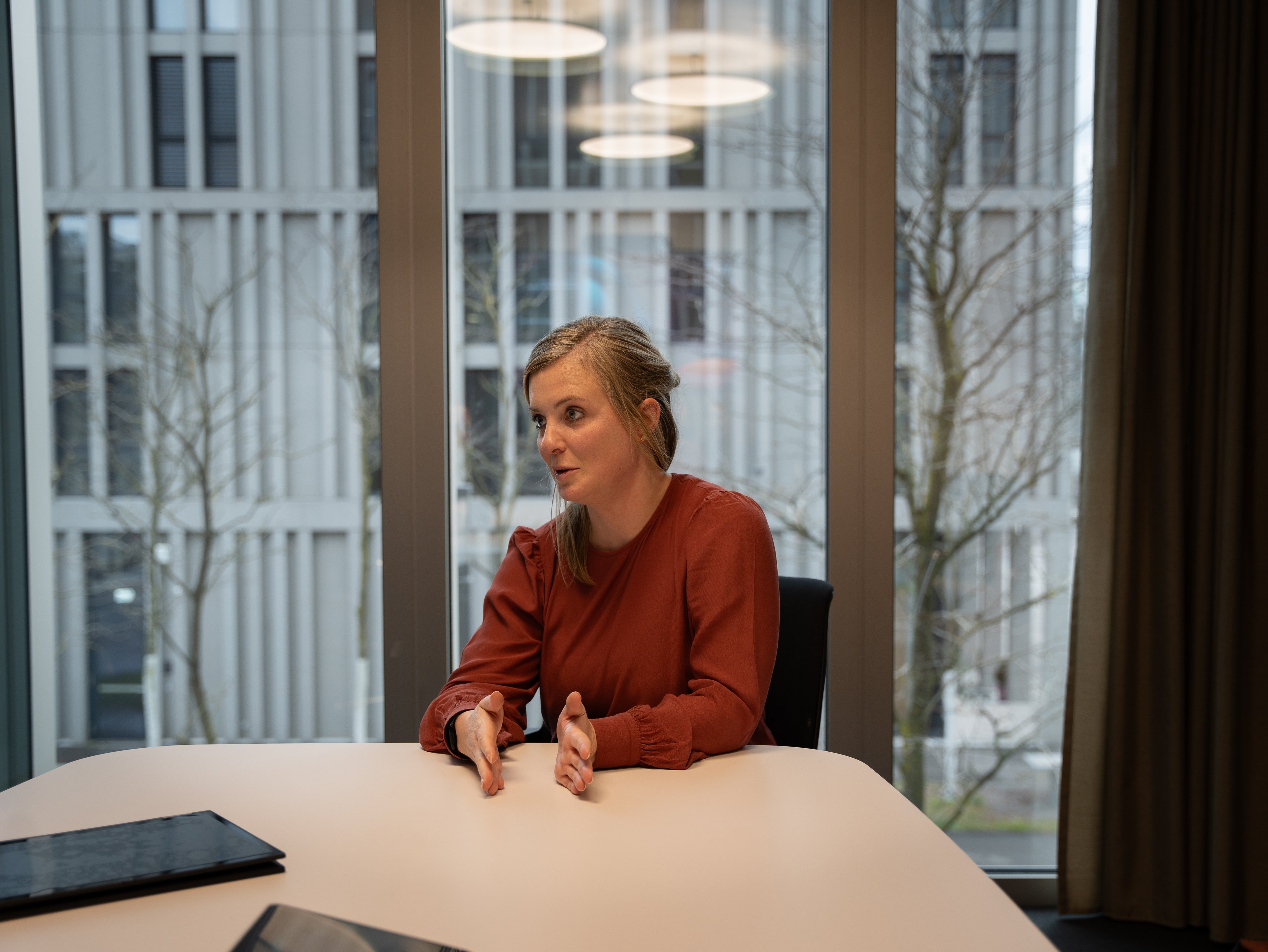 Sandra Schwander während des Interviews, sie gestikuliert mit den Händen und schaut den Redaktor an. Im Hintergrund sieht man durch die grossen Fenster den Bahnhofs Wankdorf und Gleise. Das Gespräch findet im Hauptsitz der SBB statt. 