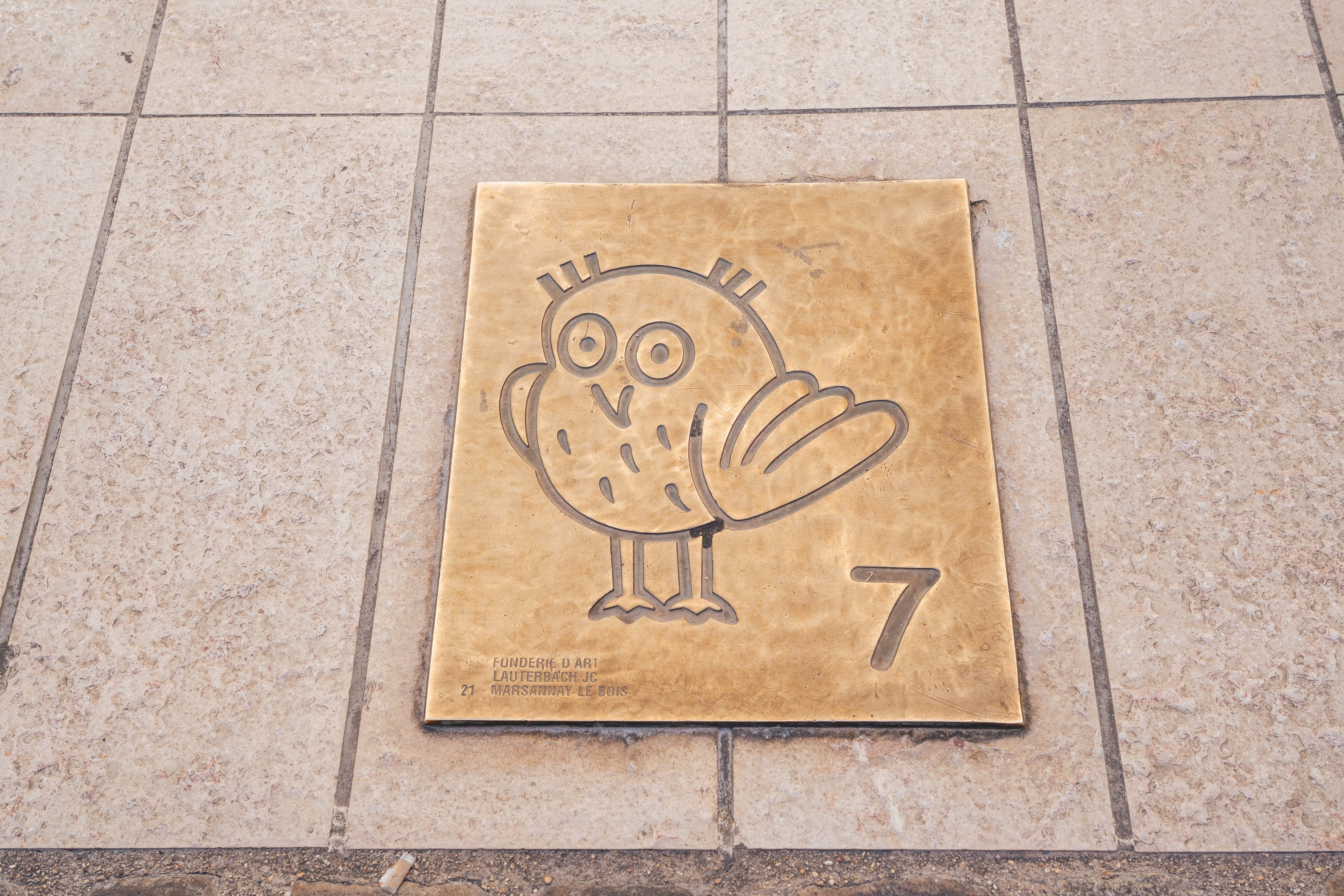 Eine Eule und die Zahl sieben ist auf Metall eingraviert. Die Plakette ist auf dem Boden.