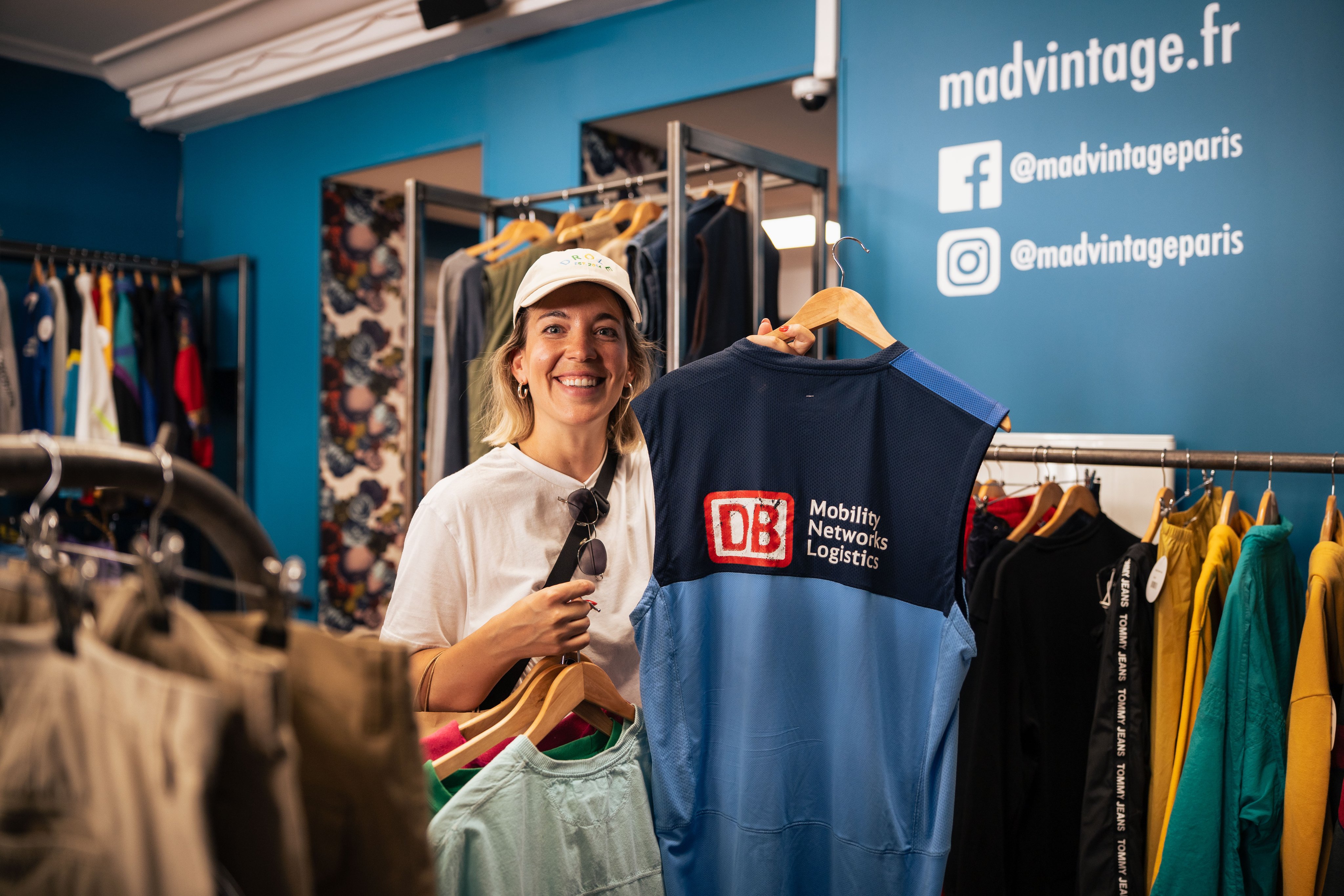 Eine Frau hält in einem Vintageladen ein DB-T-Shirt in der Hand.