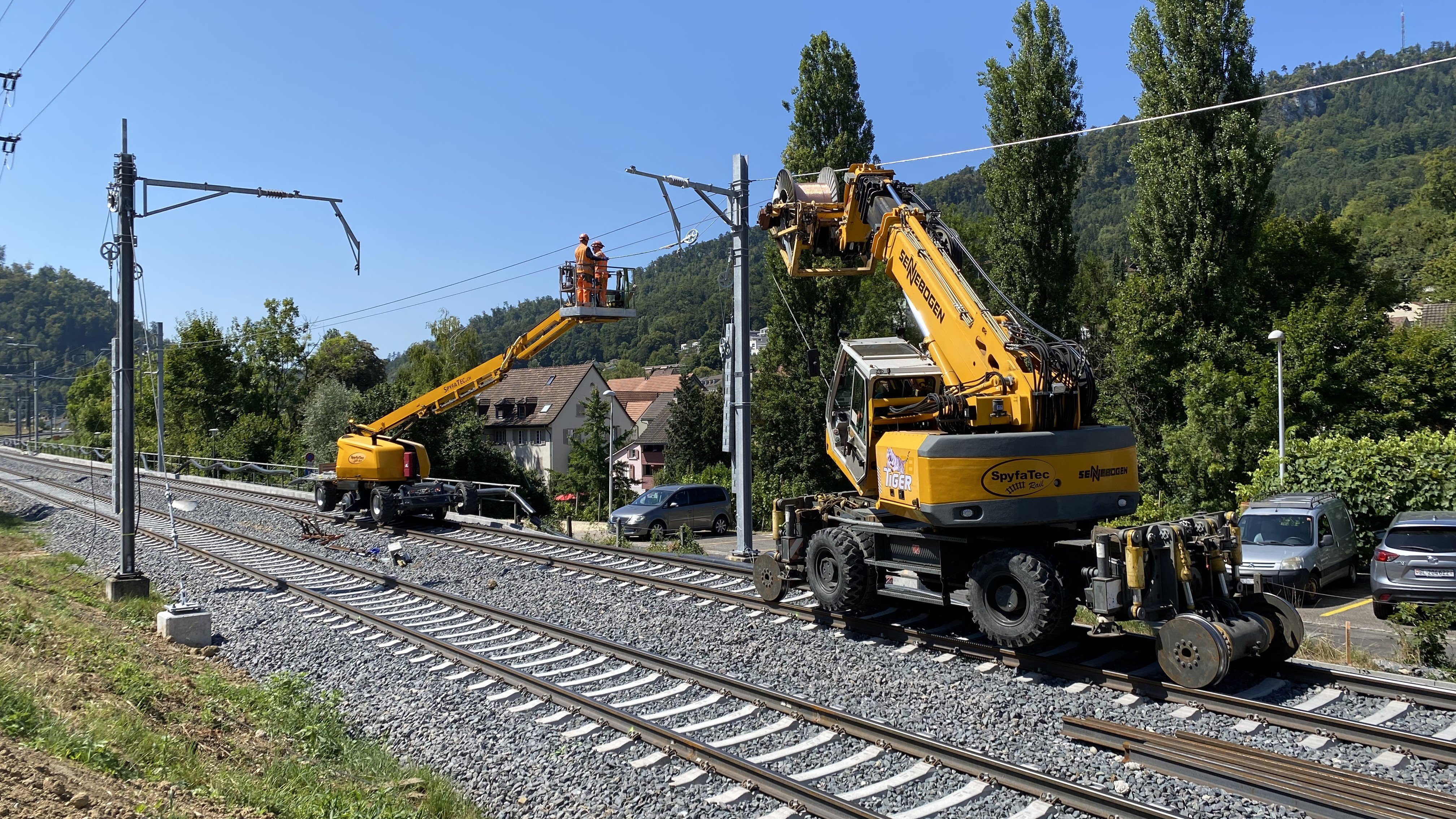 Zwei Schienenkranfahrzeuge, von denen aus Mitarbeitende die den Fahrdraht montieren.