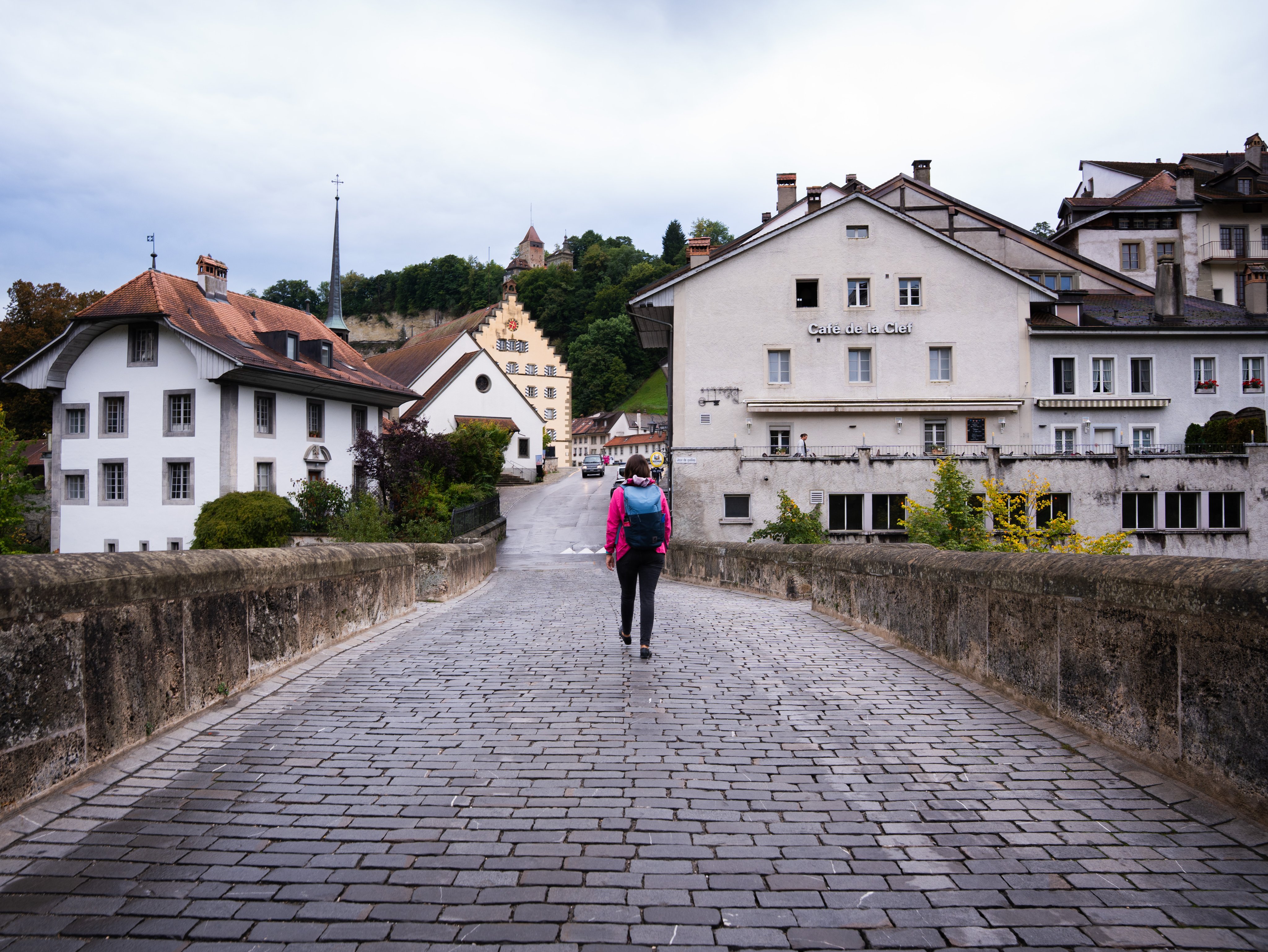 Ein Mensch von hinten auf einer Strasse mit Pflastersteinen, im Hintergrund Häuser.
