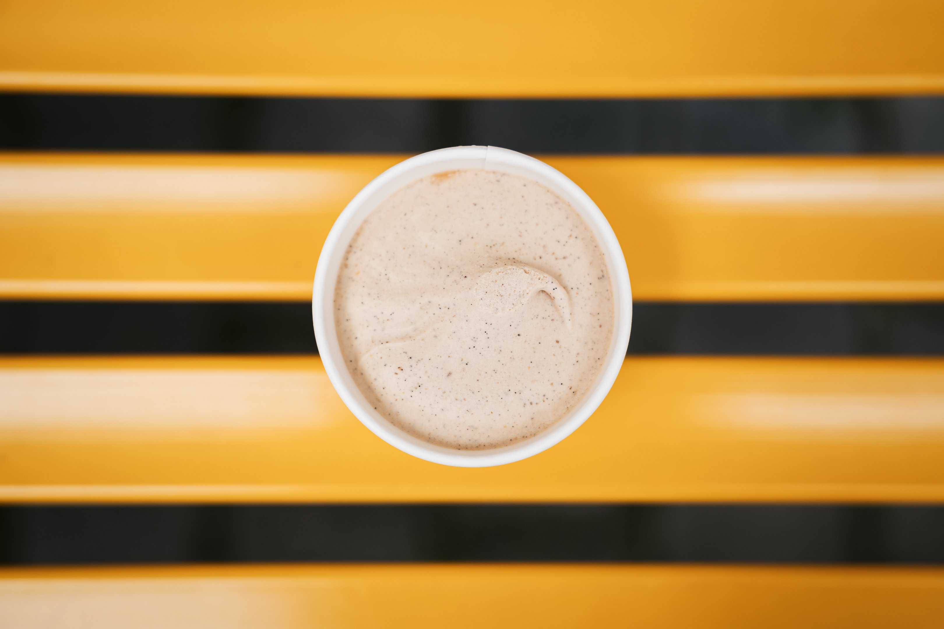 Ein kleiner Becher mit Vanille-Rooibos-Glace gefüllt auf einer gelben Sitzbank.