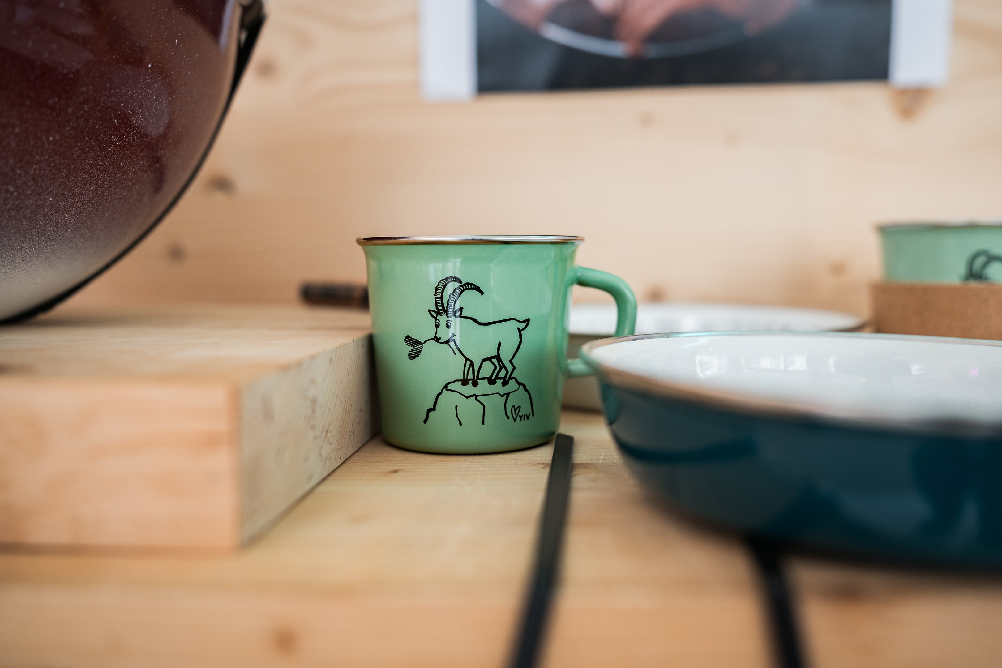 Eine grüne Tasse aus Emaille mit einem Steinbock verziert.