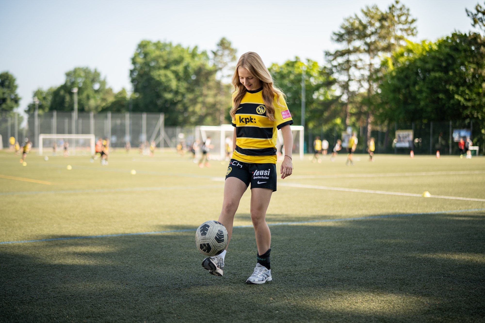 Une femme en tenue de sport jonglant avec une balle sur le pied sur un terrain de football.