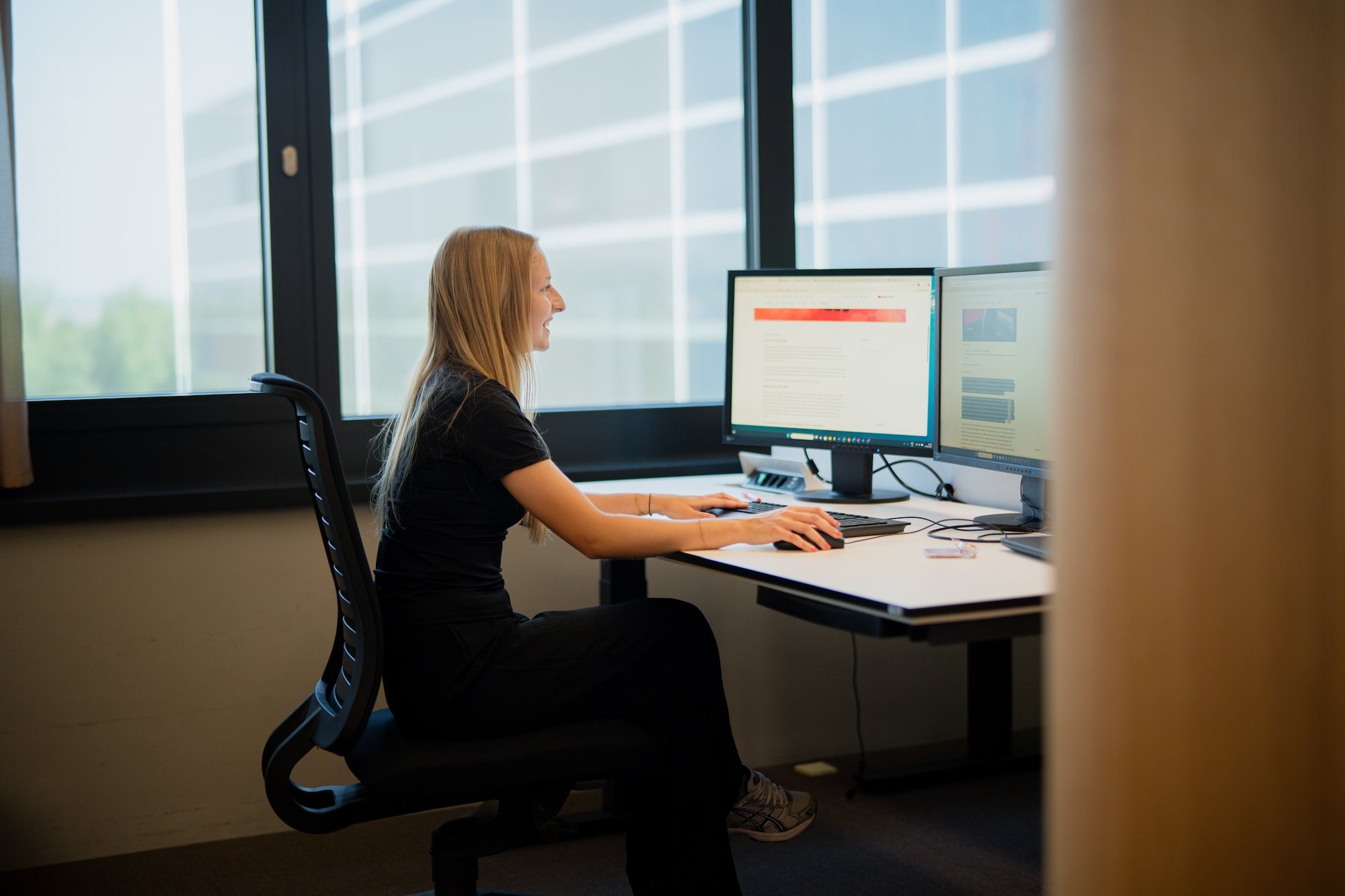Une femme est assise à un bureau sur lequel sont posés deux écrans.