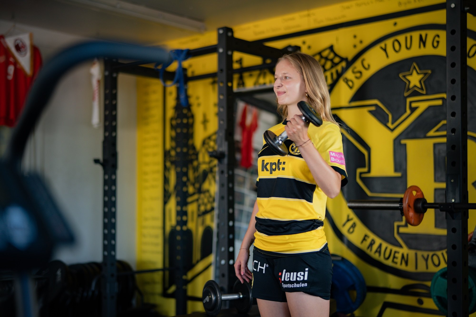 Une femme en tenue de sport soulève un haltère avec sa main gauche.