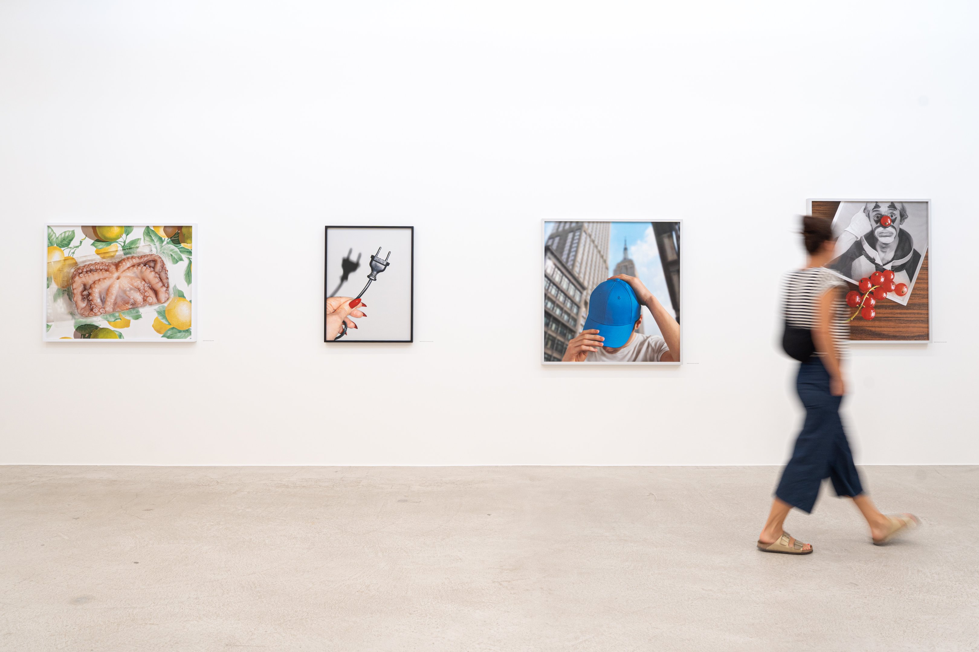 Vier gerahmte Fotos auf weisser Wand, Frau geht daran vorbei.