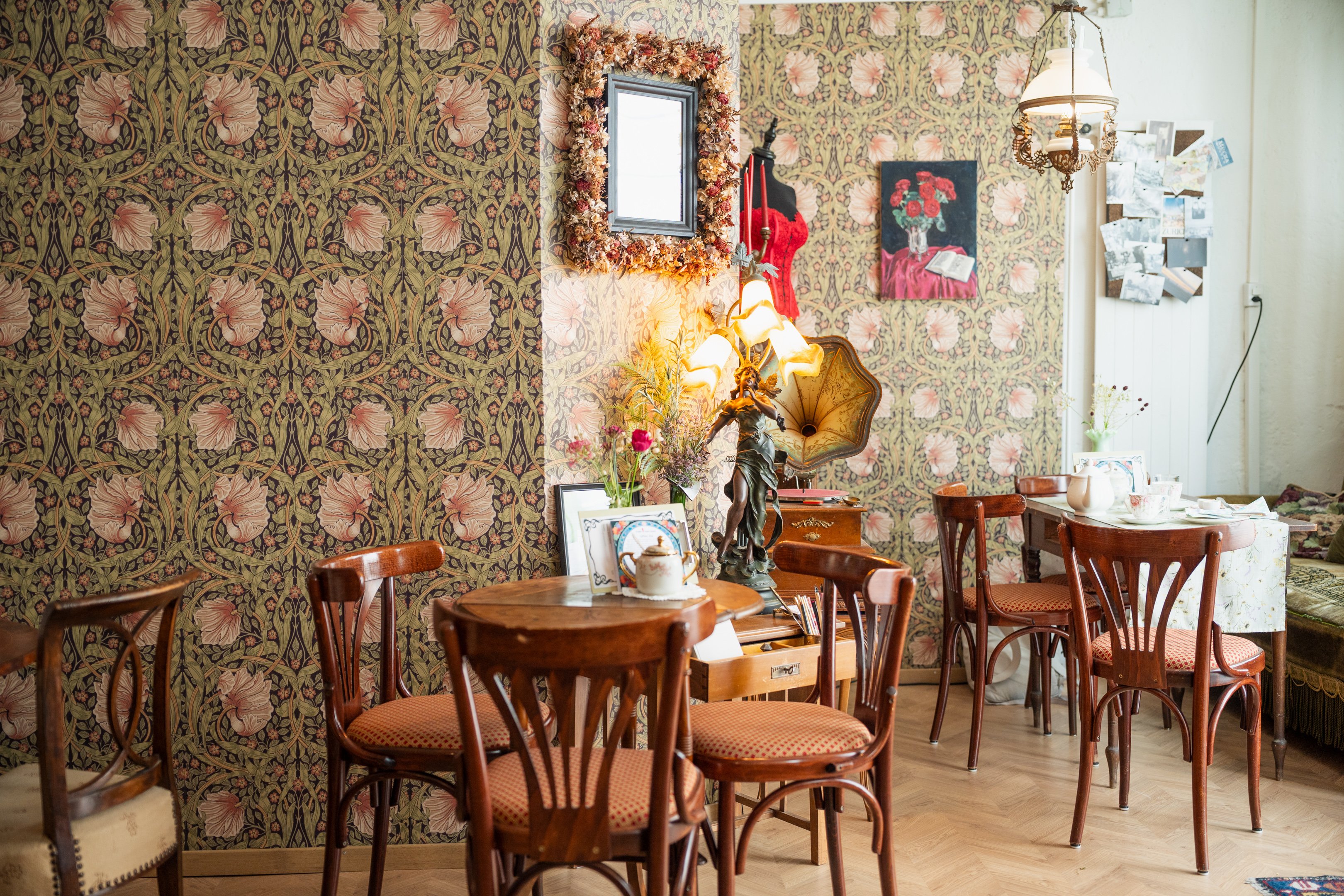 Antike Tische und Stühle im Raum des Cafés, vor blumig tapezierter Wände.